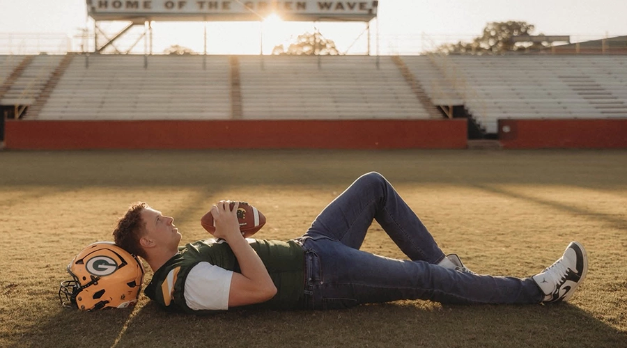 Jackson lying on football field holding football and resting head on helmet