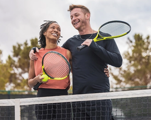 Couple holding tennis rackets on court